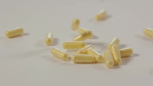 gelbe Medikamententabletten, die in Zeitlupe auf eine weiße, saubere, reine Oberfläche fallen