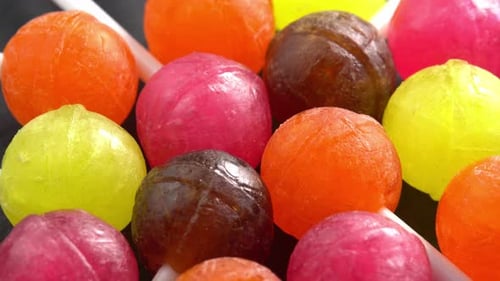 Colorful lollipops or candy bonbons on a stick rotating on black plate in macro top view sun light