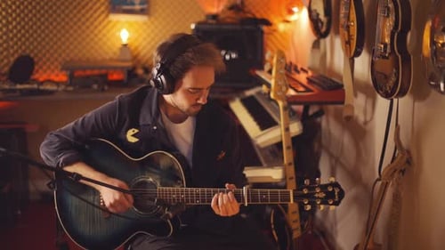 A young brunette musician man is learning how to play and record guitar music in a home recording st
