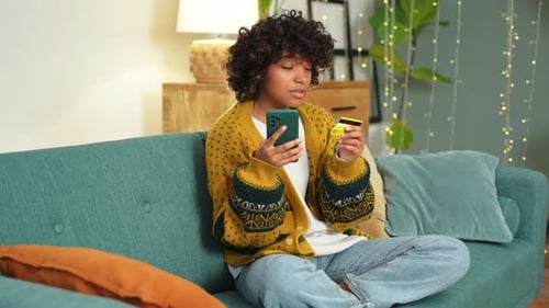 African American Woman Shopping Online Holding Smartphone Paying with Gold Credit Card Girl Sitting