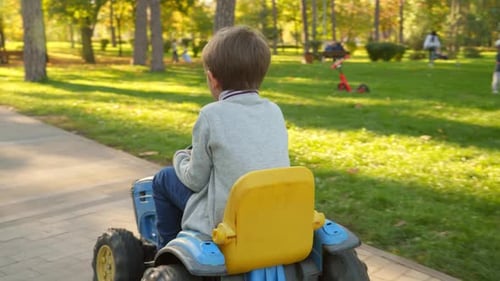 Little boy having fun while driving electric toy tractor in autumn park. Kids playing in park