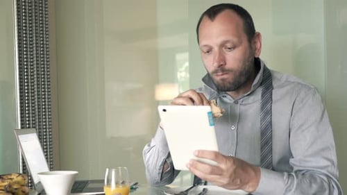 Man Eating Sandwich and Using Tablet Indoors
