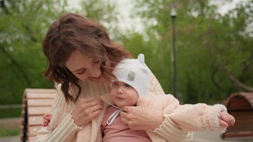 Mother Adjusting Baby's Clothing on Park Bench