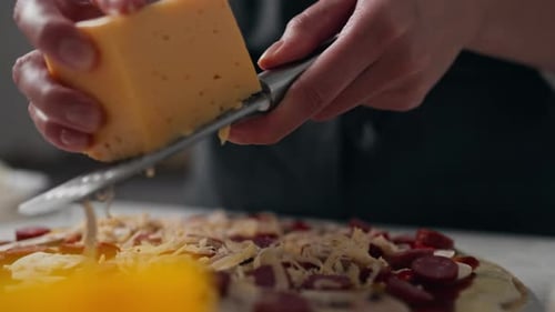 Chef grating hard yellow cheese on prepared pizza for baking, grating cheese on pizza grater