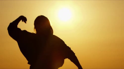 Silhouette of Woman with Arms Raised at Sunset