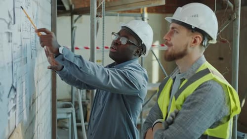 Engineer Explaining Architectural Drawings to Building Contractor on Site