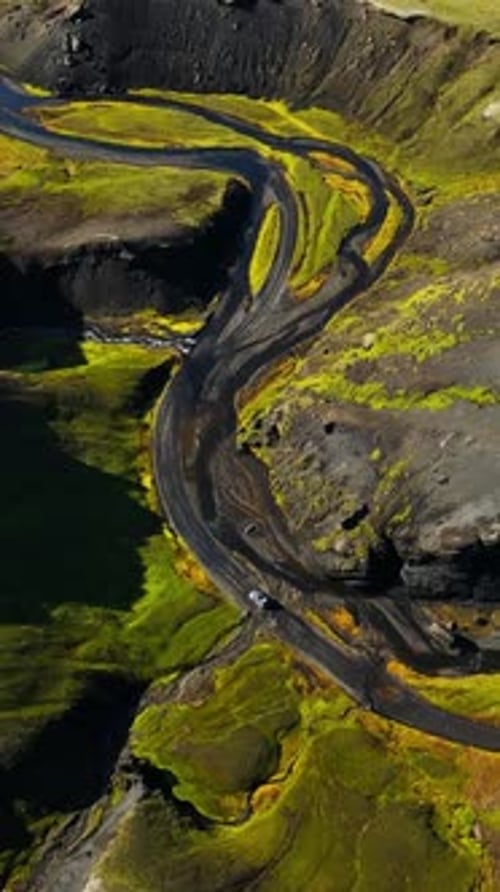 Vertical drone shot of a 4x4 driving through a remote Icelandic highland river crossing, winding
