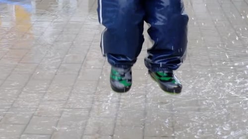 Close Up Slow Motion Shot of Legs Boy Jumping in Muddy Puddle Making Splash Rubber Boots Happy