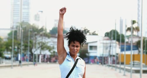 Woman Raises Fist in Air in Urban Setting