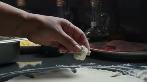 Chef adding pieces of cheese to pizza dough