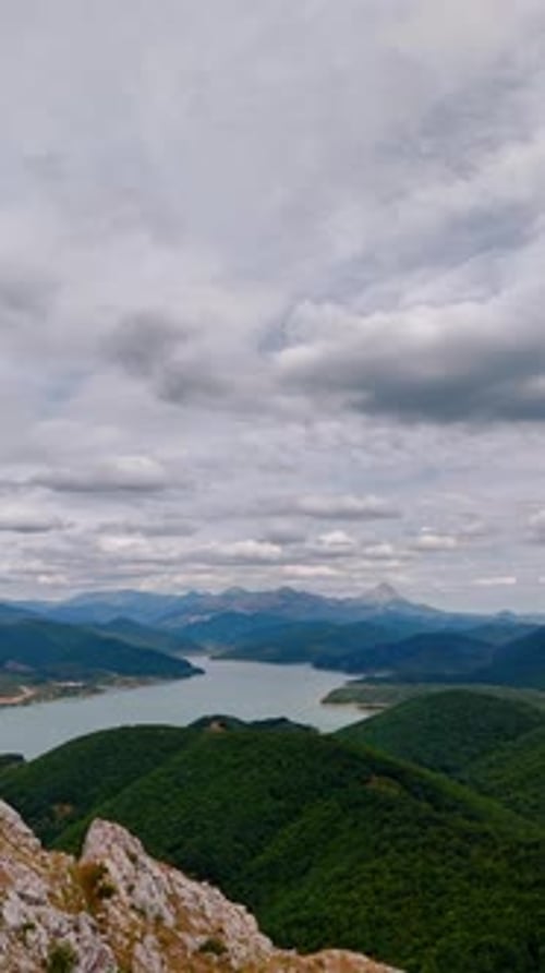 Thick green woods covering the mountainous landscape. Peaceful waterscape is among the rocks