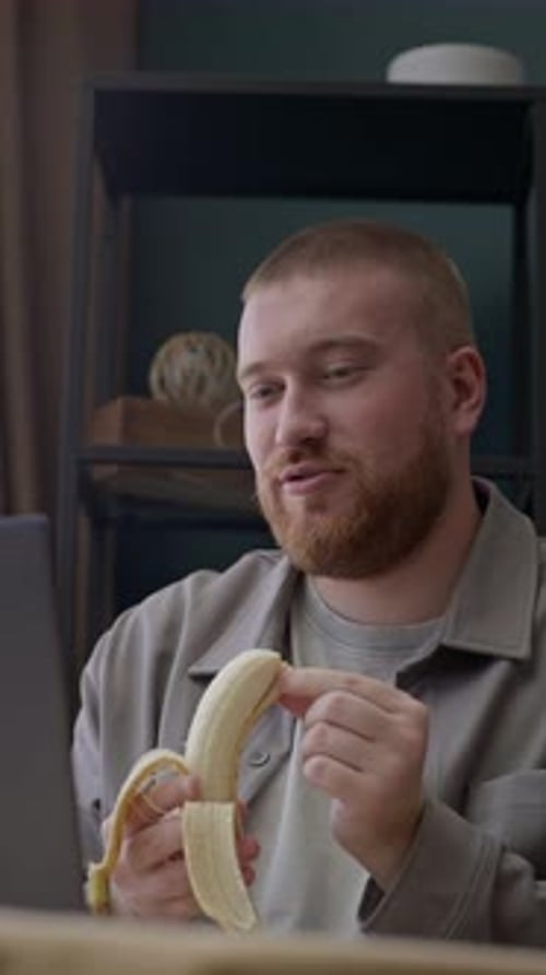 Young adult eating a banana indoors at desk