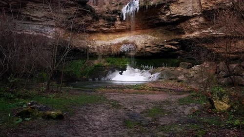 Kleiner Wasserfall mit Eisportionen auf nassen Felsen und viel Grün