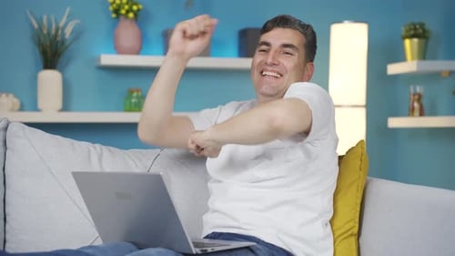 Man Celebrates Success on Laptop While Relaxing on Couch