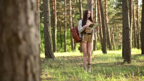 Young woman standing with map and looking for direction in the forest. Conception of travel