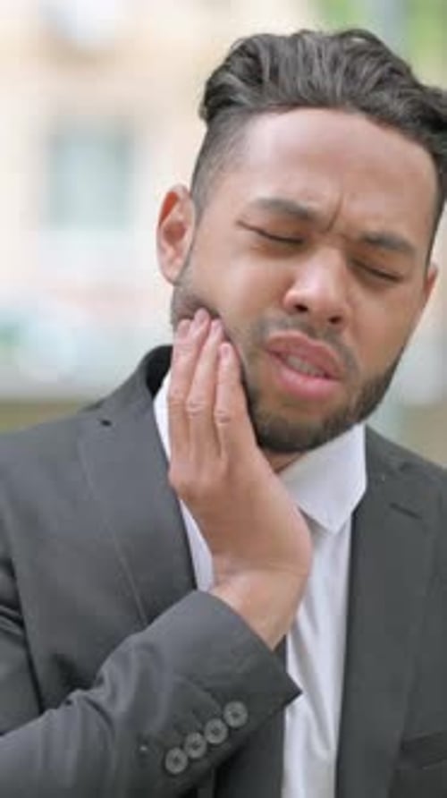 Man in Suit Experiencing Tooth Pain Outdoors