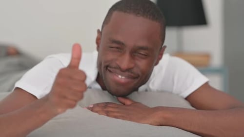 Gros plan d'un homme africain faisant les pouces en l'air alors qu'il est allongé sur le ventre dans son lit