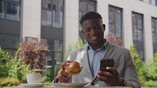 Man with Burger Using Phone Outdoors