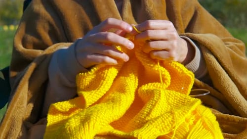 Woman Knitting Bright Yellow Yarn Outdoors on Sunny Day