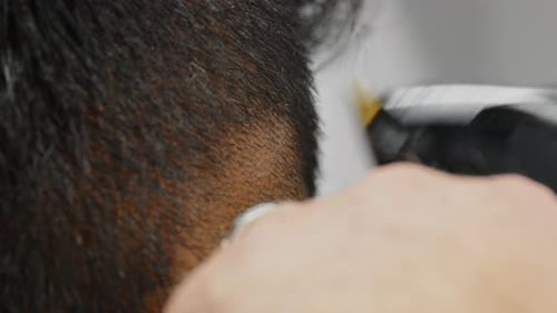 Ein Barbier reinigt die verblassende Seite der Haare eines anderen Mannes mit einer Haarschneidemaschine und rasiert sich dabei direkt auf die Haut.