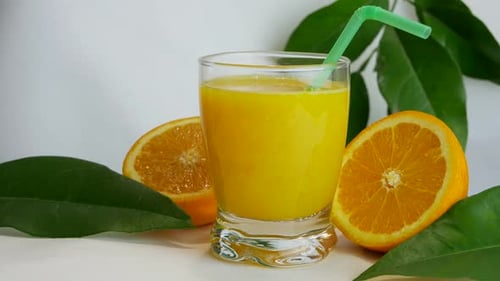 Close up studio shot of full glass of orange juice and orange halves, slow pan