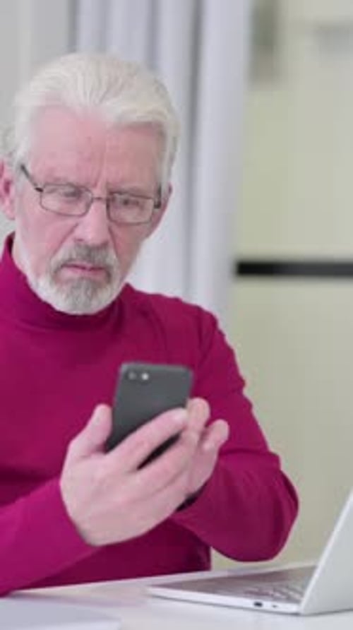 Senior Man Using Mobile Phone Indoors at Desk