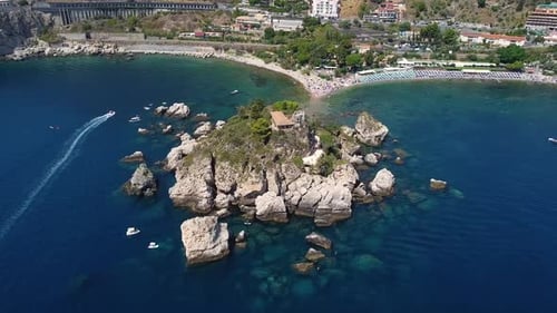 Aerial drone shot zooming into Isola Bella, Taormina in Sicily, with boats cruising past, blue sea,