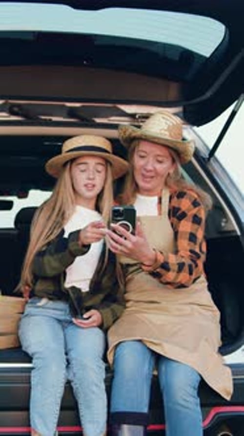 Woman and Teen in Car Hatch Looking at Phone