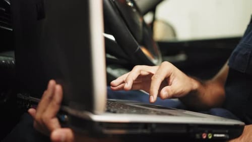 Cropped View of Bearded Male Mechanic Sitting Inside Car Using Laptop Recording