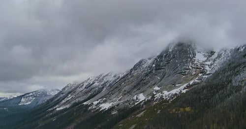 Rugged Rocky Mountainside with some snow. Canadian Mountain Landscape with Trees and Dramatic Cloudy