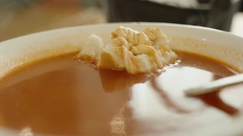 A piece of white bread with cheese in a plate of tomato soup, close-up