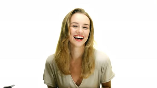 A close-up of a woman doing a full-body laugh, and brushing her hair out of her face, on a seamless