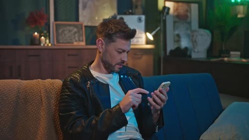 Man Using Smartphone Sitting on Sofa at Night
