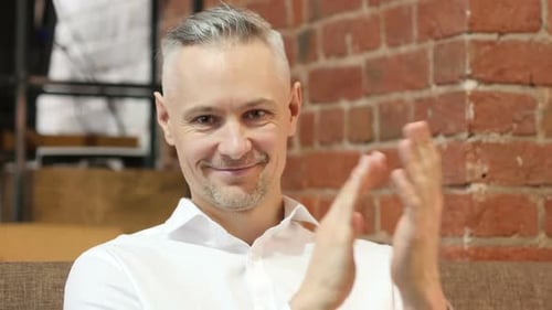 Man Clapping and Smiling Indoors by Brick Wall