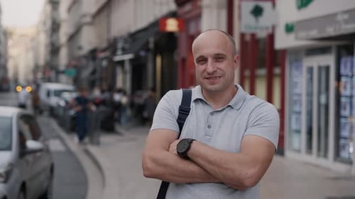 Confident Man Poses on City Street with Modern Architecture and Busy Pedestrians