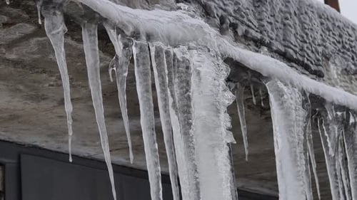 Large Melting Icicles Hanging From Concrete Roof Edge During Winter Season