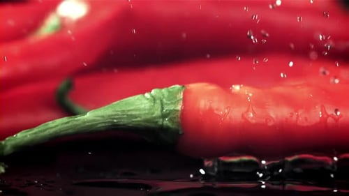 Chili Peppers fallen auf einen nassen schwarzen Tisch, gefilmt mit einer Hochgeschwindigkeitskamera mit 1000 Bildern pro Sekunde