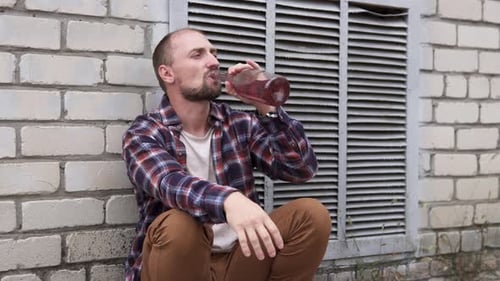 A depressed guy drinks alcohol on the street. Feeling lonely and hungover.