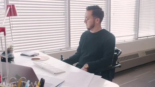 Creative businessman with beard works at desk in modern office using wheelchair