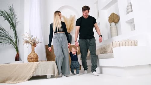 Couple holding a baby by hands walk by the room.