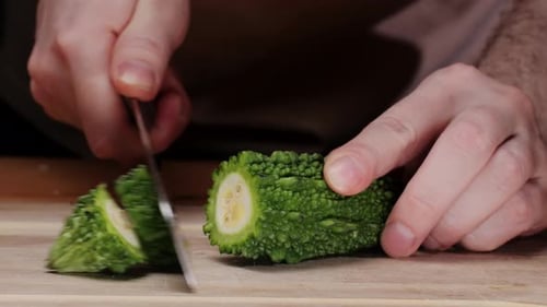 Couper une gourde amère sur un bureau en bois au couteau, gros plan d'un légume souvent utilisé comme ingrédient