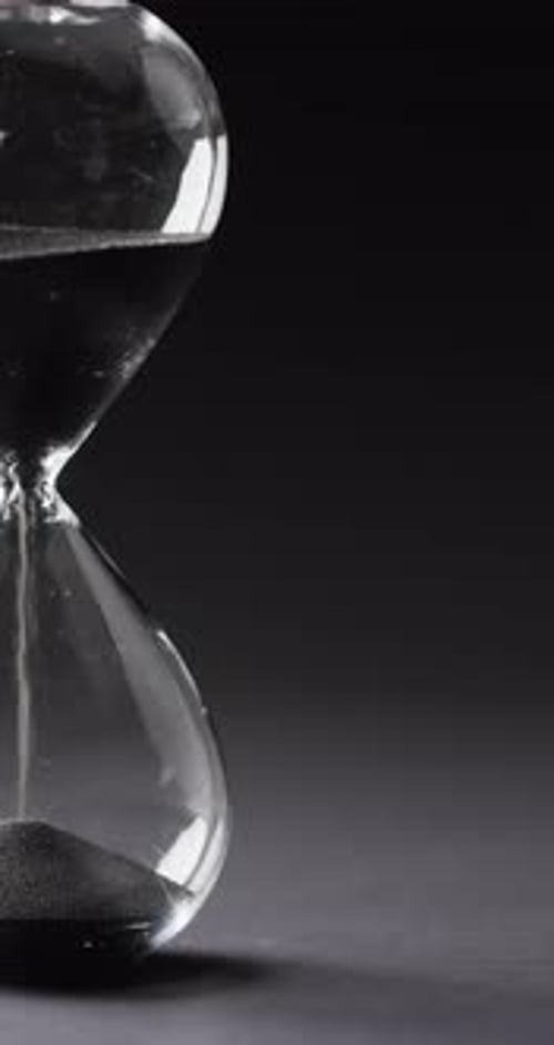 Vertical video of hourglass with sand pouring, copy space on black background