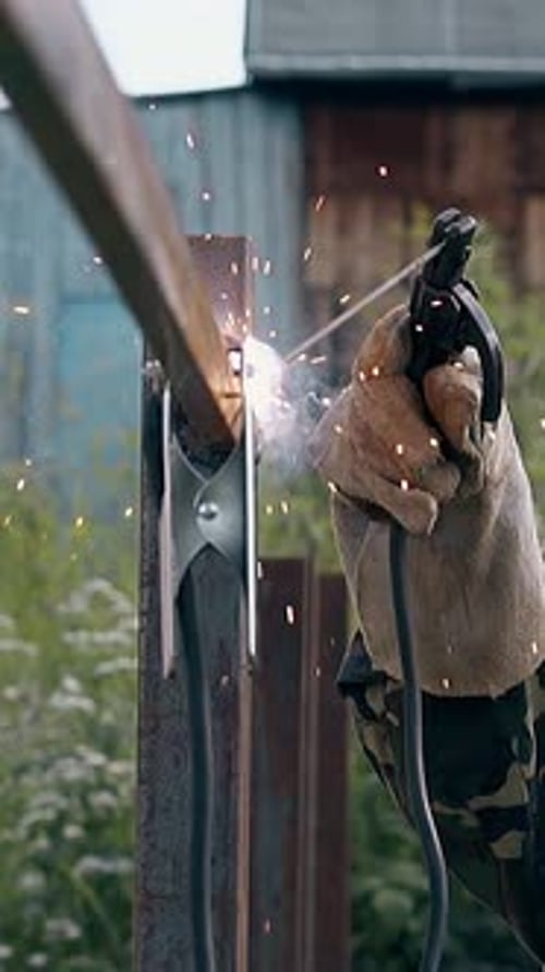 Slow Motion Side View Handyman Welds Carcass of Fence