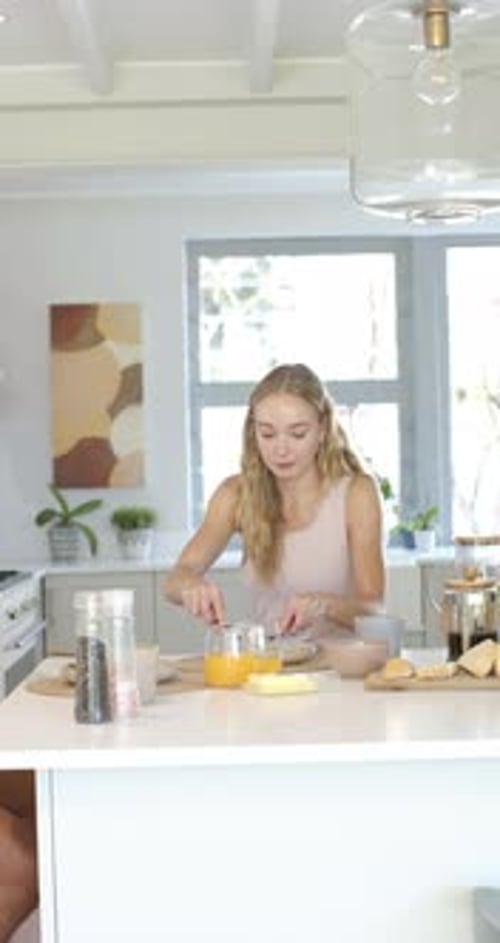 Vidéo verticale : Femme assise sur une île avec OJ préparant le petit déjeuner, étalant et remuant