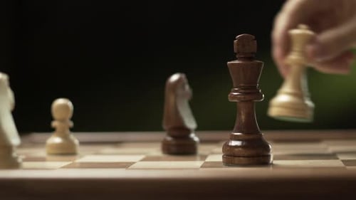 Bei einem Filmmusik Schachschuss bewegt die Hand die Schachfigur von Königin zu König, macht Schachmatt und fällt