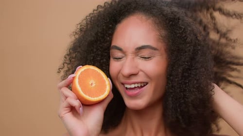 Estudio de retratos femenino sonriente mujer afroamericana sosteniendo medio fresco y saludable juego de frutas de naranja