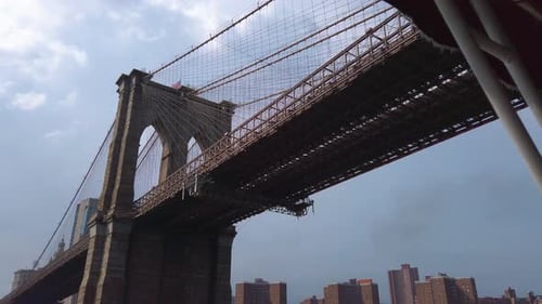New York Brooklyn Bridge, low angle on a cloudy day, driving through underneath, bridge looming upwa