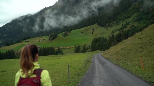Woman hiking down dirt road in Grindelwald Switzerland as train passes
