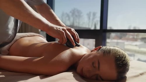 Entspannende Hot-Stone-Rückenmassage in ruhiger Spa-Umgebung mit beruhigender Berührungstherapie mit natürlichem Tageslicht