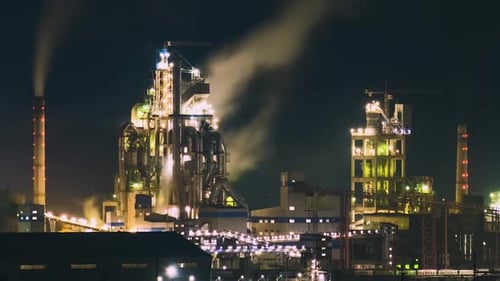 High Concrete Structure of Cement Factory with Tower Crane and Smoking Chimney at Night Industrial